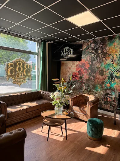Lounge-Bereich des 385-Ink-Studios mit Chesterfield-Sofas in Cognac, türkisem Velvet-Pouf und goldenem 385-INK-Logo am Fenster.
